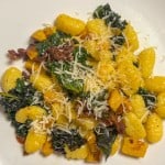A plate of gluten-free gnocchi with butternut squash, prosciutto, and kale in herbed-butter sauce