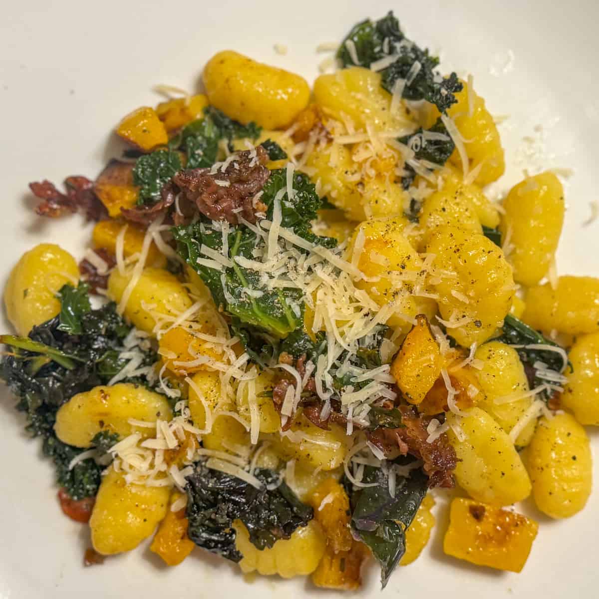 A plate of gluten-free gnocchi with butternut squash, prosciutto, and kale in herbed-butter sauce
