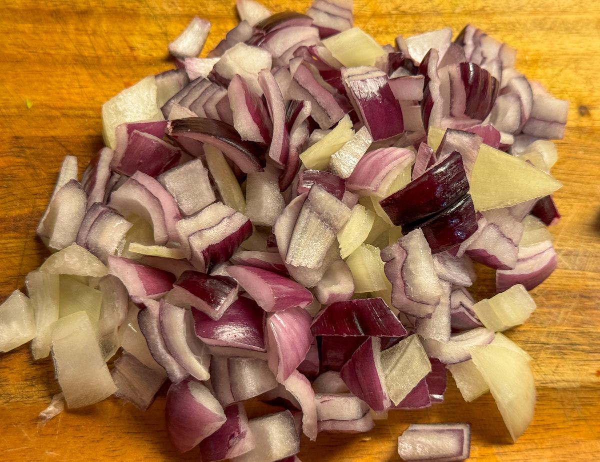 Approximately 1 cup of diced red and yellow onion on a wood cutting board 